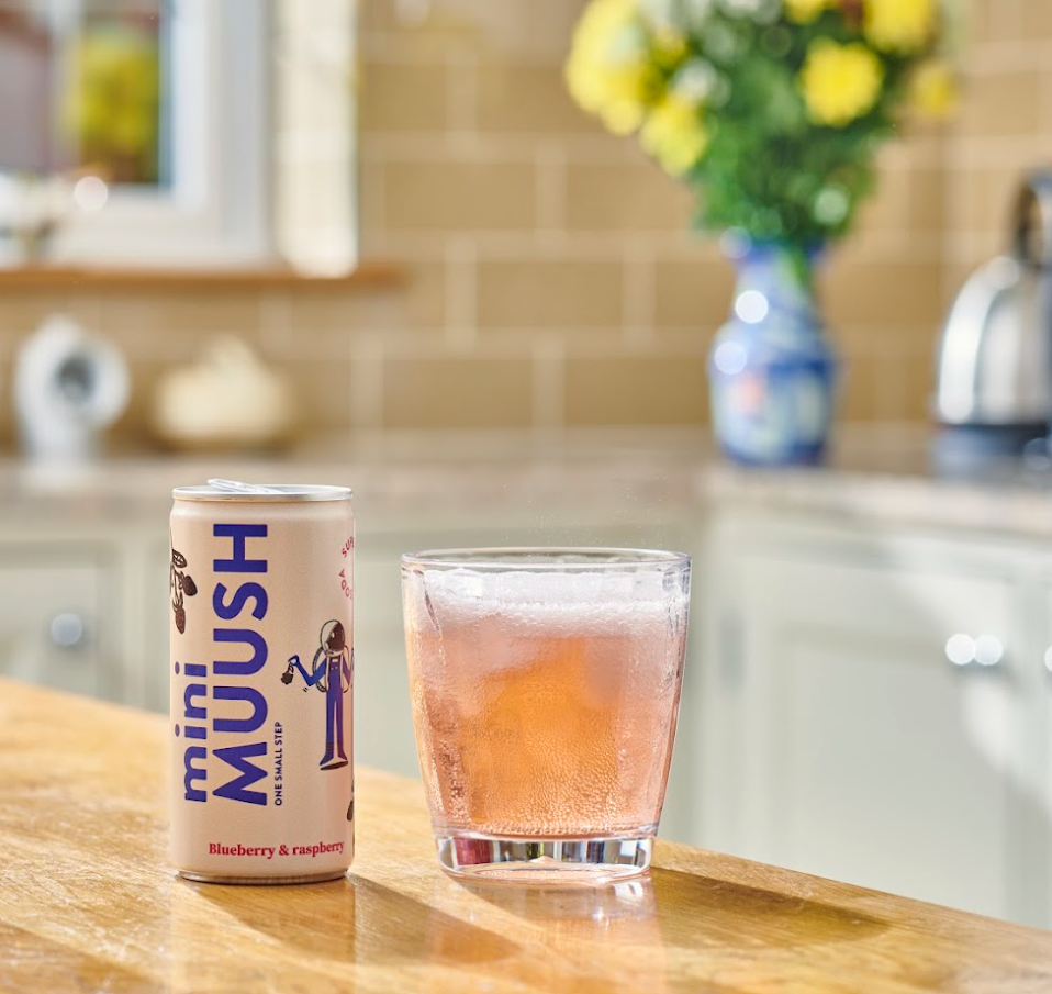 A can of miniMUUSH Blueberry & Raspberry flavor drink next to a glass of the beverage on a kitchen countertop.