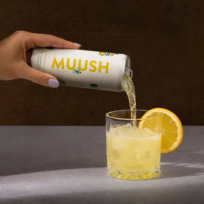 Hand pouring a can of MUUSH Sicilian lemonade in a glass with a lemon garnish 