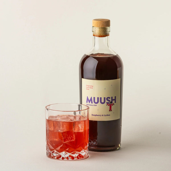 Bottle of MUUSH Raspberry and Lychee Elixir bottle with a glass of Raspberry and Lychee spritz on a light background