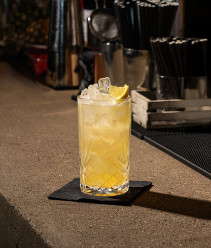 Cocktail made with MUUSH SICILIAN LEMON ELIXIR  with a lemon wedge  garnish on a bar counter
