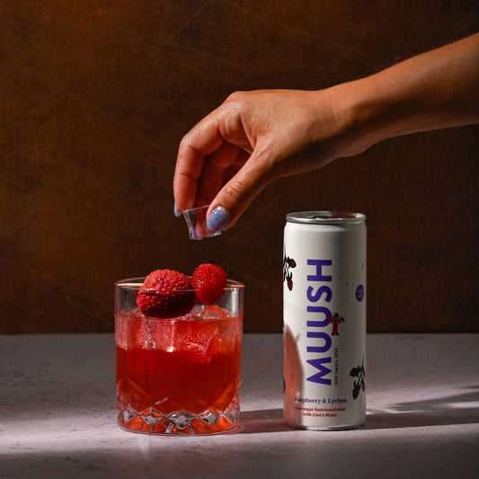 A MUUSH Raspberry & Lychee can besides a glass of the same low sugar drink with a raspberry and Lychee garnish