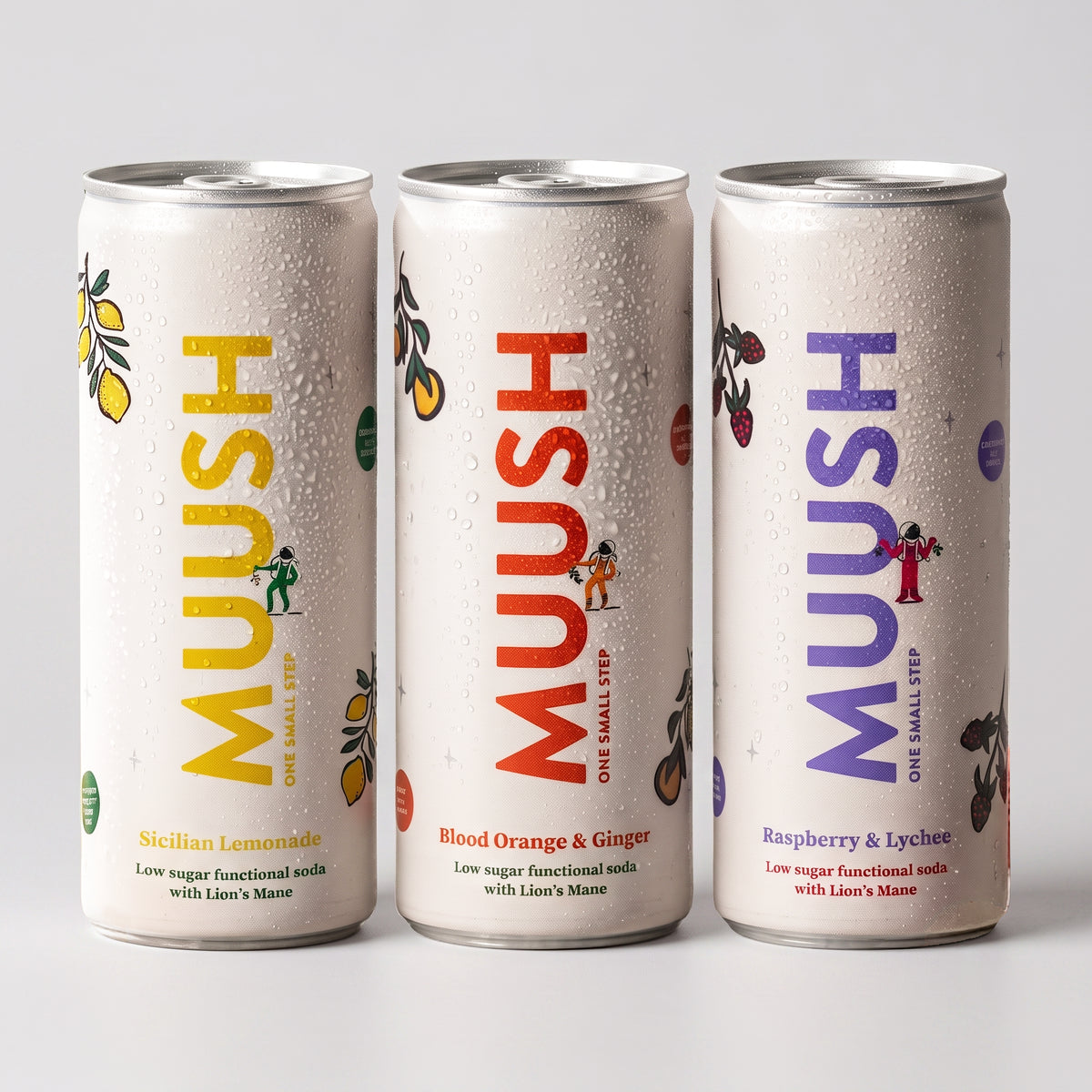 Three Muush soda cans on a light gray background, showing the Sicilian Lemonade, Blood Orange & Ginger, and Raspberry & Lychee flavors with colorful vertical branding and fruit illustrations.